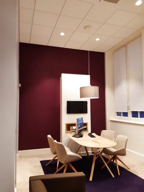 Bureau de réception client d'une agence bancaire à Orléans avec mur d'accent prune, écran mural et table ovale en bois